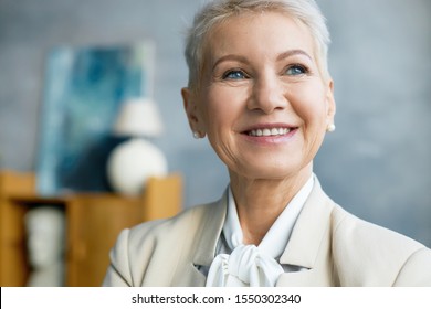 Close Up Image Of Beautiful Mature Caucasian Female CEO With Bonde Pixie Hairstyle Smiling Broadly And Looking Up Thinking About Future Business Plan And Goals, Her Eyes Expressing Confidence