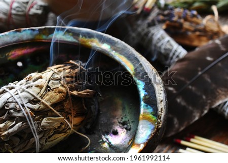 A close up image of a burning white sage smudge stick, healing crystals, and sacred feather. 