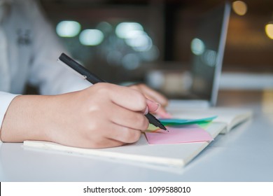 Close Up Image Of Business Hand Writing On An Adhesive Note And Pick Post It At Table In Office, Focus On Hand And Pen.