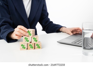 A Close Up Image Of Bussines Woman Woman Stacking Wooden Blocks In Her Work Enviroment. Office Interior Laptop, Glass Of Water And Notebook On White Desk.