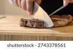 The close up image of a chef cutting medium rare grilled beef steak with chef knives on a wooden chopping board.