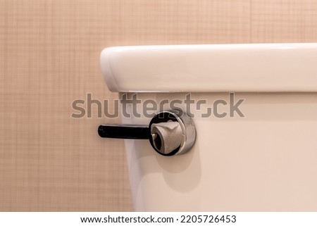 Close up image of a chrome toilet flush lever with a reflection of toilet paper.