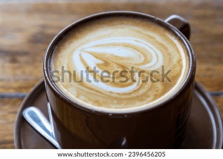 Close up image of coffee cup with flat white with milk froth and wooden table in blurred background