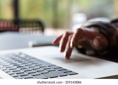 Close Up Image Of Computer And Hand Of Person Scrolling Touch Pad With Focus On Keyboard And Hotel Cafe Interior On Background