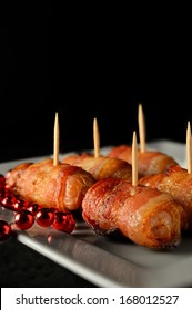 Close up image of cooked cocktail sausages, called pig's in blankets. Small savoury sausages wrapped in a blanket of smoked streaky bacon. The perfect appetizer for a Christmas party. Copy space.