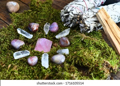 A close up image of a crystal energy healing grid on moss with various smudge sticks.
