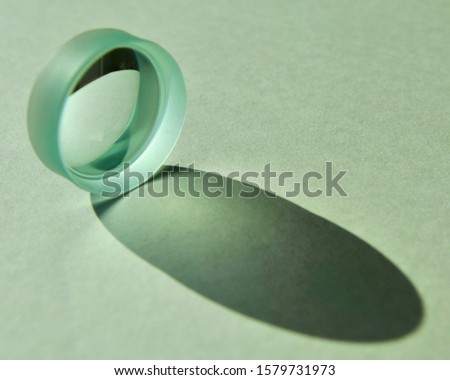 Close up image of daylight shine through clear circular concave lens with refection and refraction of light and cast shadow on white textured paper
