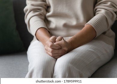 Close up image elderly woman feels nervous anxious or lonely put clenched hands on laps sitting on couch indoors. Older patient of nursing home, senile diseases and geriatric, declining years concept - Powered by Shutterstock