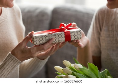 Close up image elderly womans hands holding present, receiving wrapped gift box from young daughter or grandchild. Millennial girl congratulating mature mom or granny with Mothers day or birthday.