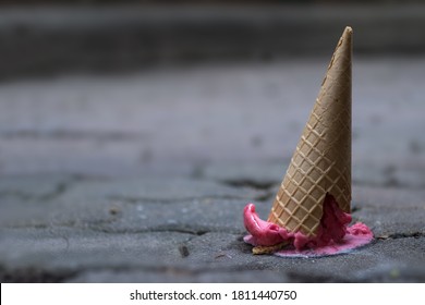 Close up image of fallen pink sorbet ice cream with cracking cone on the old cement ground background. Selective focus and copy space. 