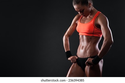 Close up image of  female in sports clothing relaxing after workout on dark background. Muscular female body with sweat. Image with copyspace for text