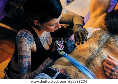Close up image of female tattoo artist makes a tattoo on a man's torso.