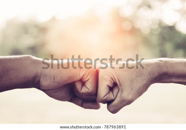 A close up image of a fist bump in vintage tone.\
Hands of young people show strength teamwork in the nature, team\
concept.