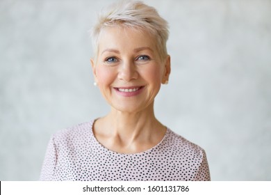 Close up image of good looking beautiful mature blonde female with blue eyes, elegant make upand pixie hairstyle smiling at camera, having confident happy facial expression, being in good mood