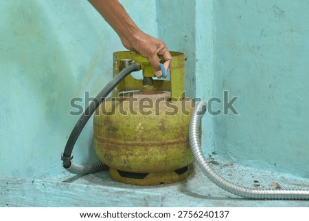Close up image of a hand installing a gas regulator on a household gas cylinder indoors representing home maintenance safety and energy use
