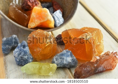A close up image of a hand made pottery bowl and red, yellow, blue, and green calcite crystals. 