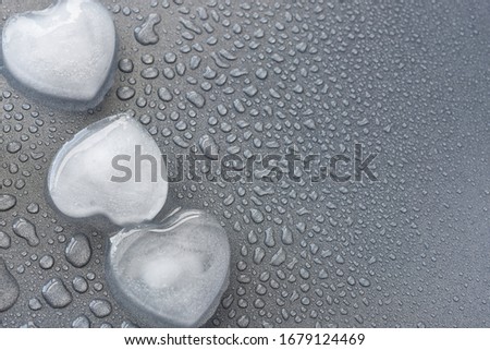 A close up image of a heart shaped ice cube melting on a grey background.