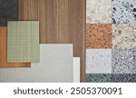 close up image of interior material samples, top view, including multi color of terrazzo stones, oak wooden laminated, wooden veneer, fabric laminateds placed on black concrete table.