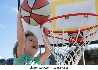 Close Up Image Of Kid Basketball Player Making Slam Dunk During Basketball Game In Outdoor Basketball Court. The Child Player Is Wearing Sport Clothes