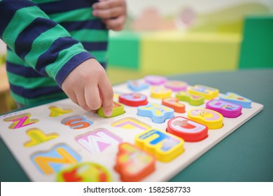 Close up image of kid hand holding colorful English alphabets puzzle toy placing in wooden block, space for text and design
