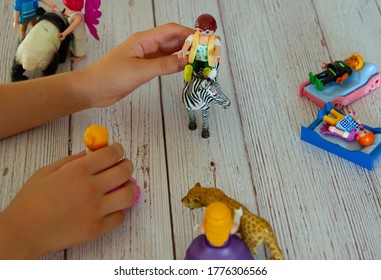 Close up image of a kid's hands as she plays with toy figures on wooden table. She creates a composition involving animal and human figurines and role plays a story out of it by moving each item.