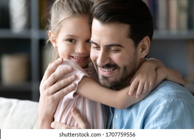 Close up image lovely little kid girl embracing young handsome daddy sitting on couch at home. Caring father snuggle daughter smiling enjoy time together feeling love devotion and affection concept - Powered by Shutterstock