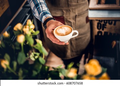 Close Up Image Of A Man Holds A Coffee With A Heart Foam Top View.