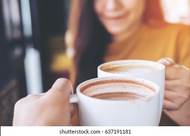 Close up image of man and woman clink white coffee mugs in cafe - Powered by Shutterstock