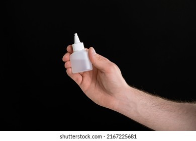 A Close Up Image Of Man's Hand Holding A Bottle Of Glue Isolated On Black Background