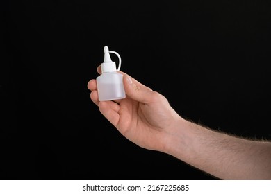 A Close Up Image Of Man's Hand Holding A Bottle Of Glue Isolated On Black Background