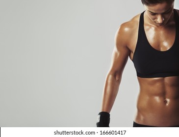 Close up image of middle eastern female in sports clothing relaxing after workout on grey background. Muscular female body with sweat. Image with copyspace for text