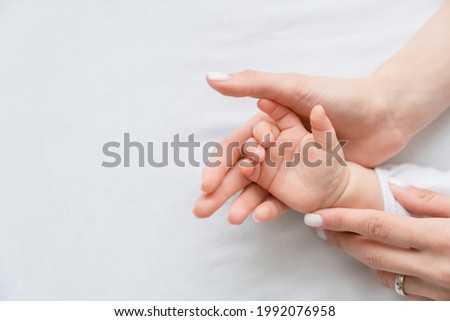 Close up image of a mother`s mom hand holding her little small toddler`s infant newborn tiny hand on white background. Childcare, motherhood concept.