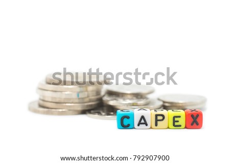 Close up image of the multicolor alphabet dices which are arranged for a word CAPEX in front of stack of coins, isolated on white background.
