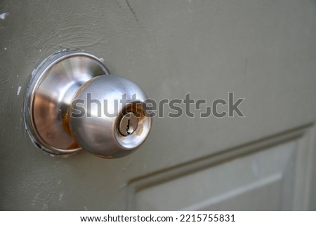 A close up image of an old and dirty metal door knob on a greyish-green painted door.