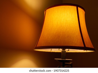 Close Up Image Of An Old Floor Lamp With Vintage Fabric Lamp Shade Creating A Peaceful Dim Warm Light Which Bounces Back From The Wall Creating A Moody Scene. Soft Light Is Ideal For Bedroom Settings.