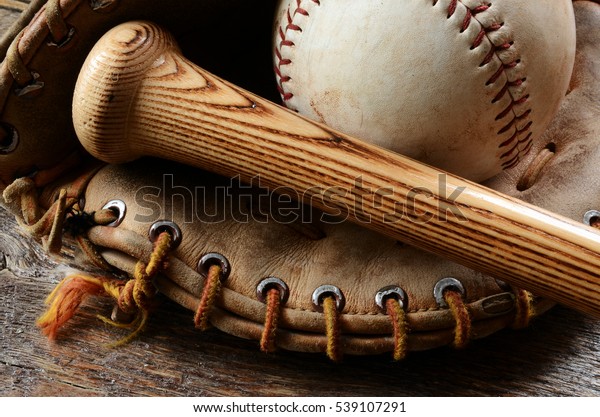 A close up image of an old used baseball, baseball\
bat, and baseball glove.