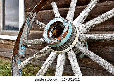 A close up image of an old wooden wagon wheel leaning on a log cabin. 