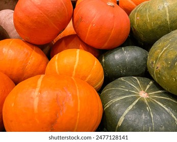 A close up image of a pile of pumpkins. The pumpkins are mostly orange, with a few green ones mixed in. The pumpkins are all different sizes and shapes. - Powered by Shutterstock