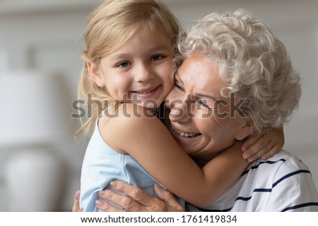 Close up image portrait happy small cutie granddaughter hugging with caring old grandmother, multi generational family relatives people snuggle to each other feeling love and strong connection concept