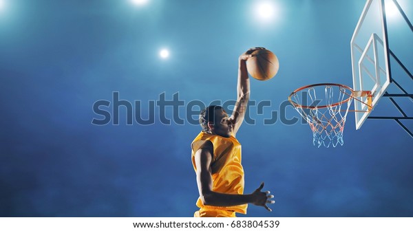 Close up image of
professional basketball player making slam dunk during basketball
game in floodlight basketball court. The player is wearing
unbranded sport clothes.