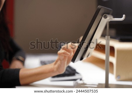 Close up image, Selective focus unrecognizable woman in mask use finger touch on screen of digital tablet on stand at workplace