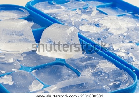 A close up image of several cracked and broken ice cubes in a blue ice cube tray. 