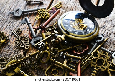A close up image of several old vintage keys with pocket watch on a dark wooden table top. 