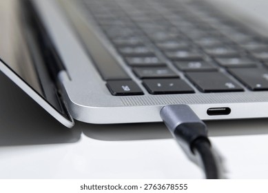 A close up image shows a USB Type C cable plugged into the side port of a laptop on a clean desk surface.