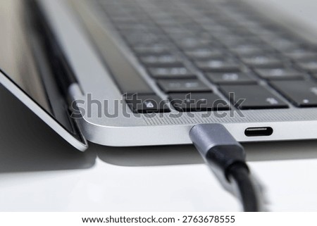 A close up image shows a USB Type C cable plugged into the side port of a laptop on a clean desk surface.