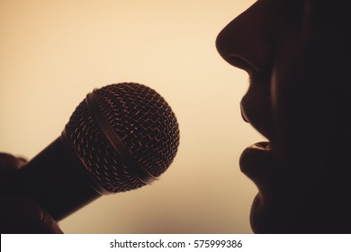 Close Up Image Of A Silhouette Of A Woman Singing To A Microphone.