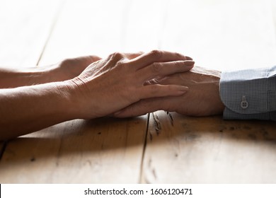Close up image spouses sit at wooden desk holding hands feeling love and strong attachment wife and husband arms together as symbol of honesty, heart-to-heart talk, give support to loved one concept
