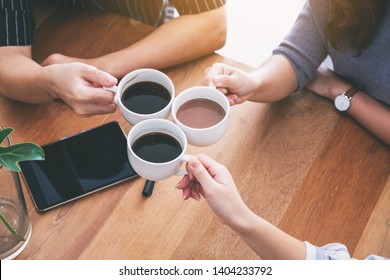 Close Up Image Of Three People Enjoyed Drinking And Clinking Coffee Cups On Wooden Table In Cafe