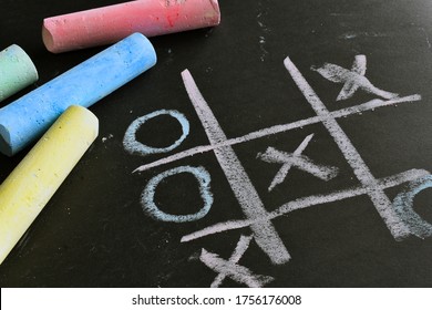 A close up image of a tic-tac-toe game done in brightly colored chalk on a black background.  - Powered by Shutterstock