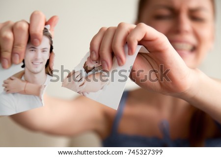 Close up image of torn into two pieces photograph of happy smiling and hugging young couple in hands of upset crying woman angry because of divorce or breakup of relations. Betrayal, jealousy concept